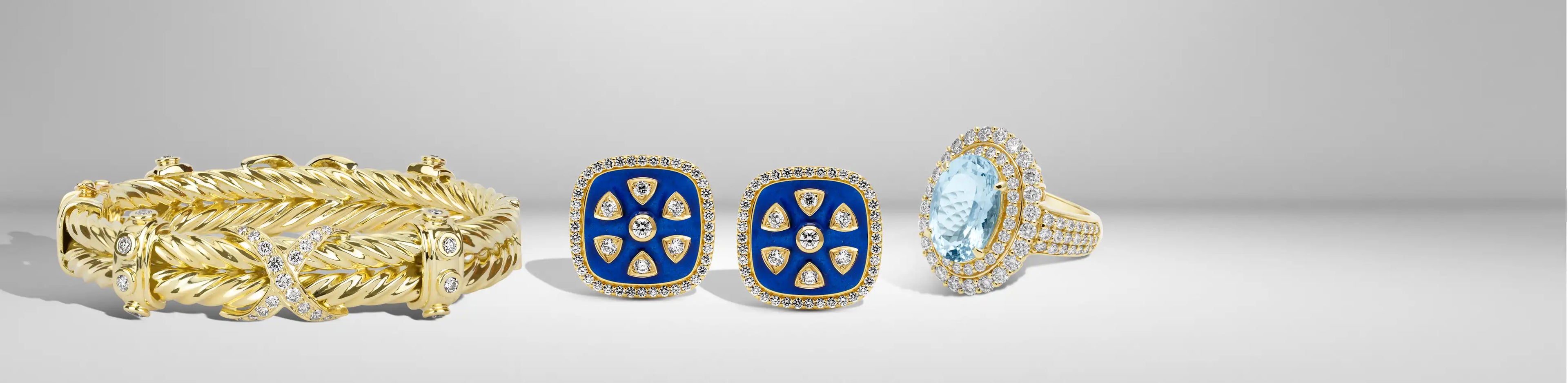 A gold cuff bracelet, blue enamel earrings, and a gemstone ring with diamond accents on a soft gray background | Singhvi Jewels All Jewelry Collection