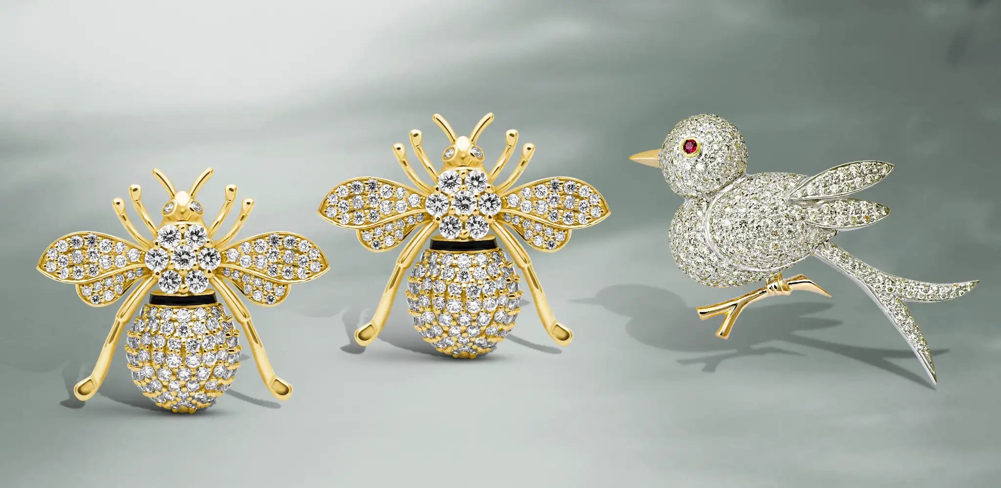 Gold bee earrings with diamond accents beside a diamond-studded bird brooch with a ruby eye on a soft gray background | Singhvi Jewels Animal Collection