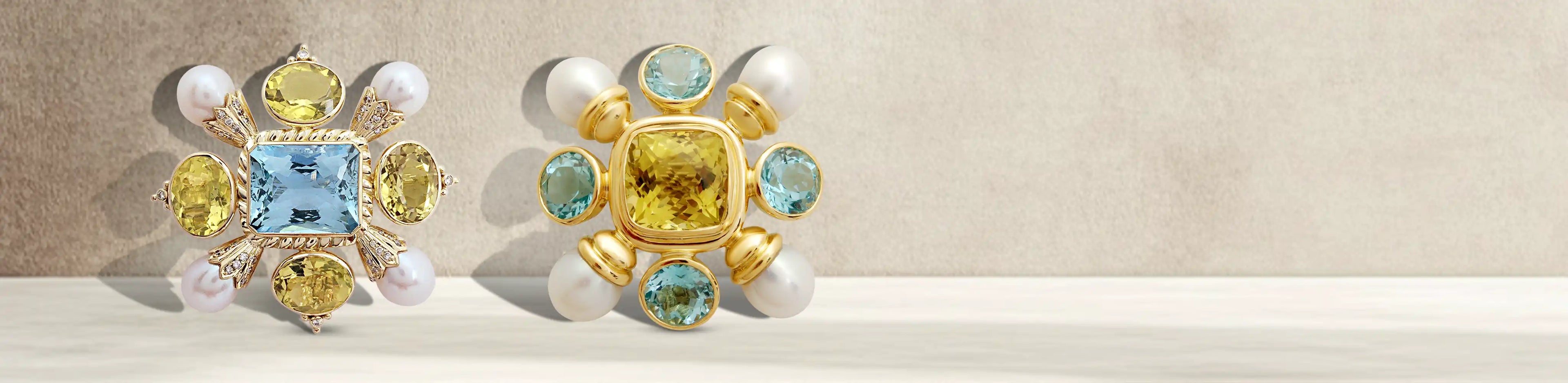 Two gold brooches with colorful blue topaz and lemon quartz gemstones, white pearl accents, and detailed geometric designs.