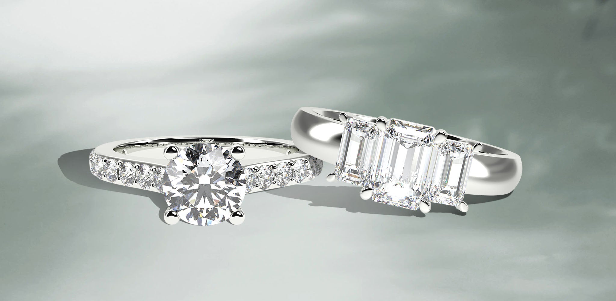 Two elegant engagement rings featuring brilliant-cut and emerald-cut diamonds on polished white gold bands against a soft gray background | Singhvi Jewels Engagement Collection