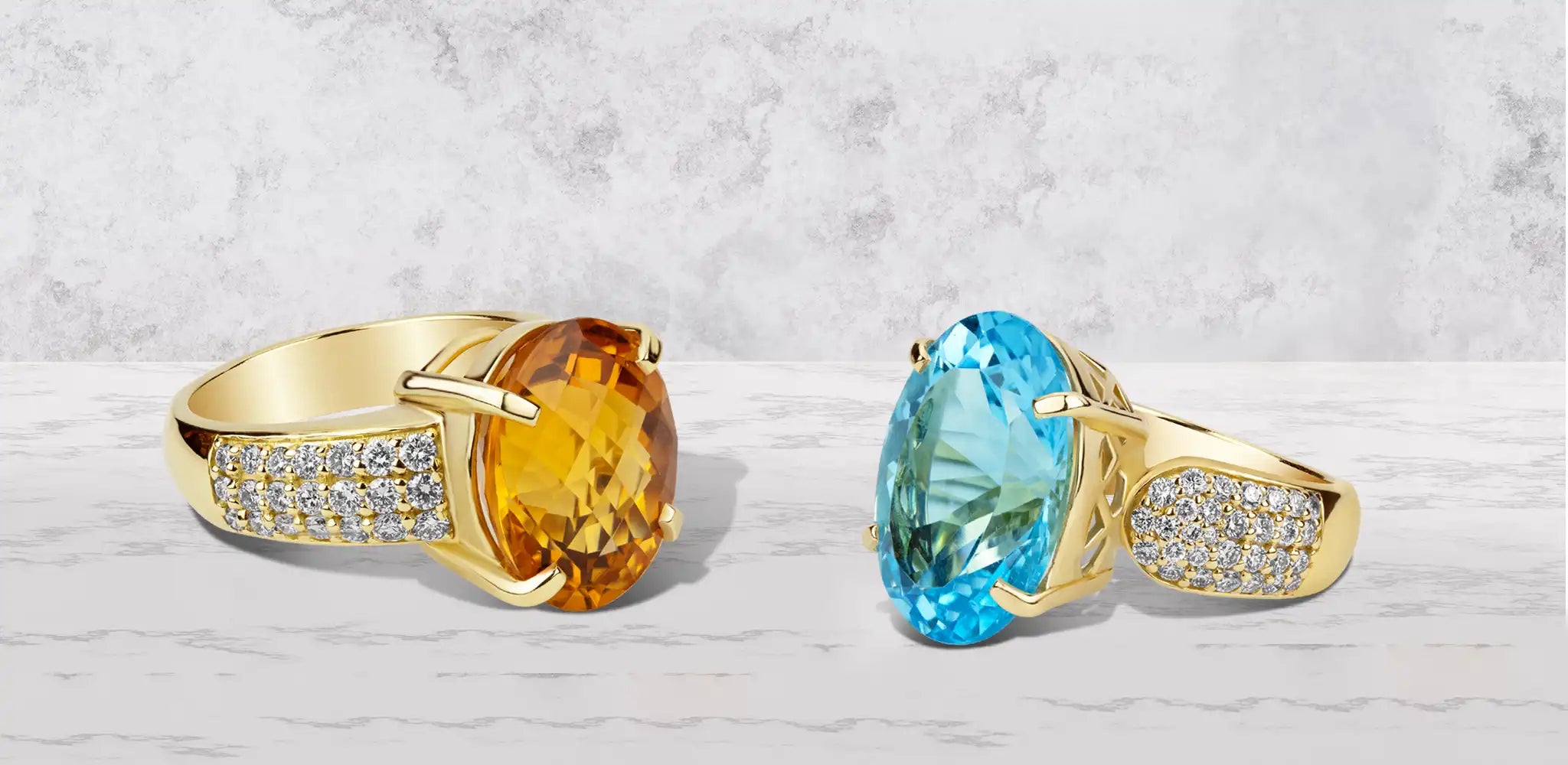 Two gold rings featuring oval citrine and blue topaz gemstones with diamond accents on the gold bands against a soft gray background | Singhvi Jewels Single Stone Jewelry Collection